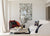 Image shows the Livius armchair in rust velvet and stained black oak in the corner of a living area. A decorative cushion also sits on the chair. The walls are white. Abstract art hangs on the wall in the background. Cream sofas and a Remy round coffee table are in the foreground. 