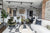 A photograph showing an open plan kitchen, dining and living area.  The Ludmila sofa sits on a black and white rug to the right of the image, a sage green velvet Mallow armchair is in the left of the image, with sage green ripple bar stools behind, a Samantha coffee table sits in front of the sofa in the centre of the image.  A dining table with Kadiev chairs in in the background to the right. Art work is hung on the walls to the right. 
